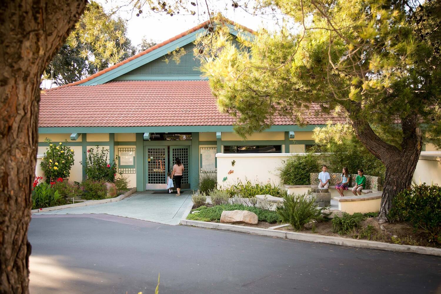 San Diego Dental Specialists office exterior with a red-tiled roof and green trim, surrounded by trees, plants, and people nearby.